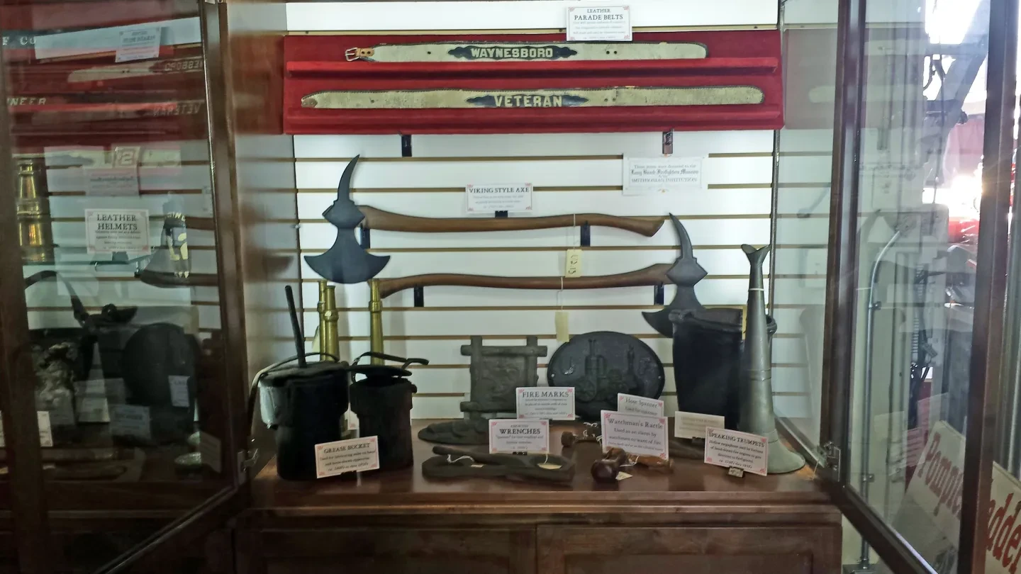 Museum display case showing Viking-style axes, fire marks, wrenches, speaking trumpet, and leather parade belts